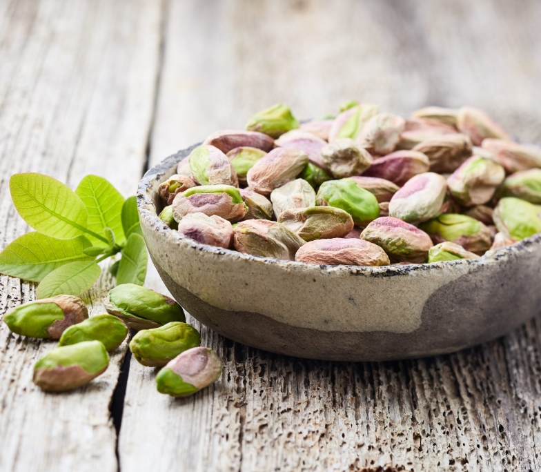 Pistachio nuts with leaves on wooden background